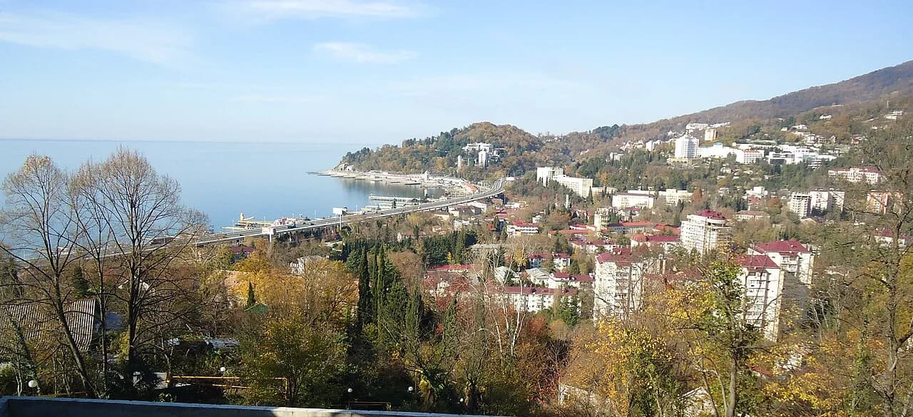 Панорама Хосты: жилая застройка на склонах холмов у моря, мыс и Чёрное море, осенние деревья